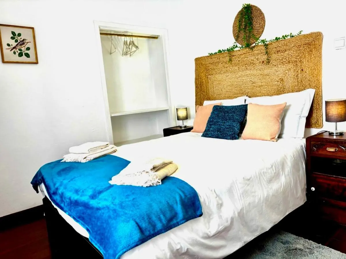 Quarto com cama de casal, manta azul e cabeceira de palha